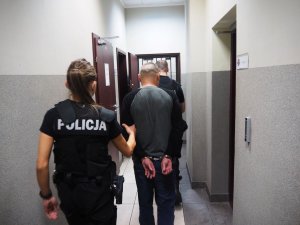 Policjantka wraz z policjantem prowadzą zatrzymanego mężczyznę korytarzem.