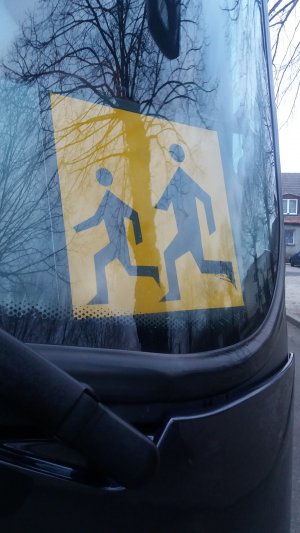 Za przednią szybą autobusu włożony jest znak w kształcie żółtego prostokąta. Na nim namalowane są postaci dwóch osób. Jest to oznaczenia przewozu dzieci.