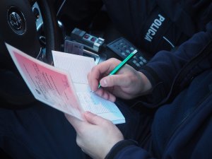 Policjant spisuje do notatnika informacje z dokumentów autobusu.