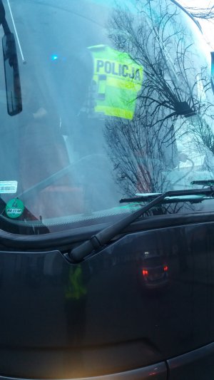 Przednia szyba autobusu przez który widoczny jest policjant w żółtej kamizelce odblaskowej.