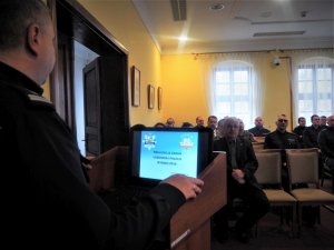 Komendant Wojewódzki Policji w Gorzowie Wielkopolskim stoi przed mównicą, na której znajduje się laptop. Na wprost niego siedzą sulęciński policjanci oraz zaproszeni goście.