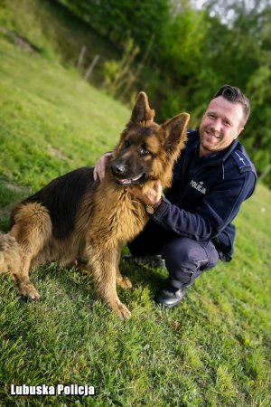 Uśmiechnięty policjant kuca przy psie Atosie