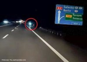 Jezdni autostrady A2. Po prawej stronie znak informacyjny. Dalej czerwonym okręgiem oznaczony jest światło. Jest to mężczyzna poruszający się pasem awaryjnym hulajnogą.