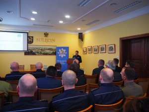 Komendant Powiatowy Policji w Sulęcinie podczas swojego wystąpienia podsumowującego wyniki pracy sulęcińskiej jednostki. Na pierwszym planie zaproszeni goście.