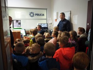 Dzieci w towarzystwie policjantów oglądają obraz z miejskiego monitoringu.