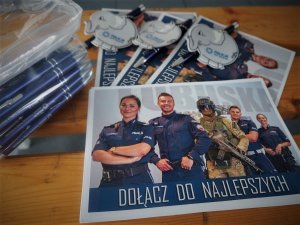 Na ławce szkolonej leżą ulotki, długopisy oraz odblaskowe breloczki promujące zawód policjanta.