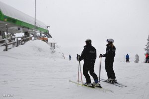 Dwoje policjantów stoi na nartach na ośnieżonym stoku przy wyciągu