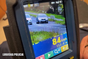 Zdjęcie ekranu ręcznego miernika prędkości ukazujące kierowcę skody, który wyprzedza inny pojazd na skrzyżowaniu. Urządzenie wyświetla także przekroczony pomiar prędkości 84 kilometry na godzinę.