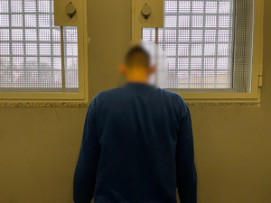Zatrzymany mężczyzna stoi tyłem do zdjęcia na tle krat policyjnej celi. Ubrany jest w granatową bluzę.
