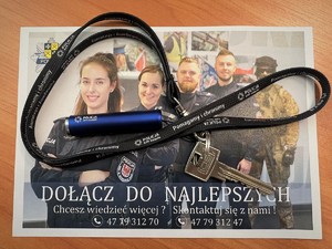 Ulotka z promocji zawodu policjanta, a na niej smycz oraz latarka z logo sulęcińskiej Policji z przypiętym kluczem do mieszkania.