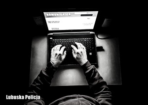 Zakapturzony mężczyzna siedzi przed laptopem, prowadząc czat na komunikatorze.