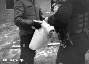 Policjant przekazuje osobie bezdomnej kołdrę i poduszkę.