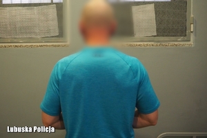 Zatrzymany mężczyzna stoi tyłem do zdjęcia w policyjnej celi na tle okratowanych okien.